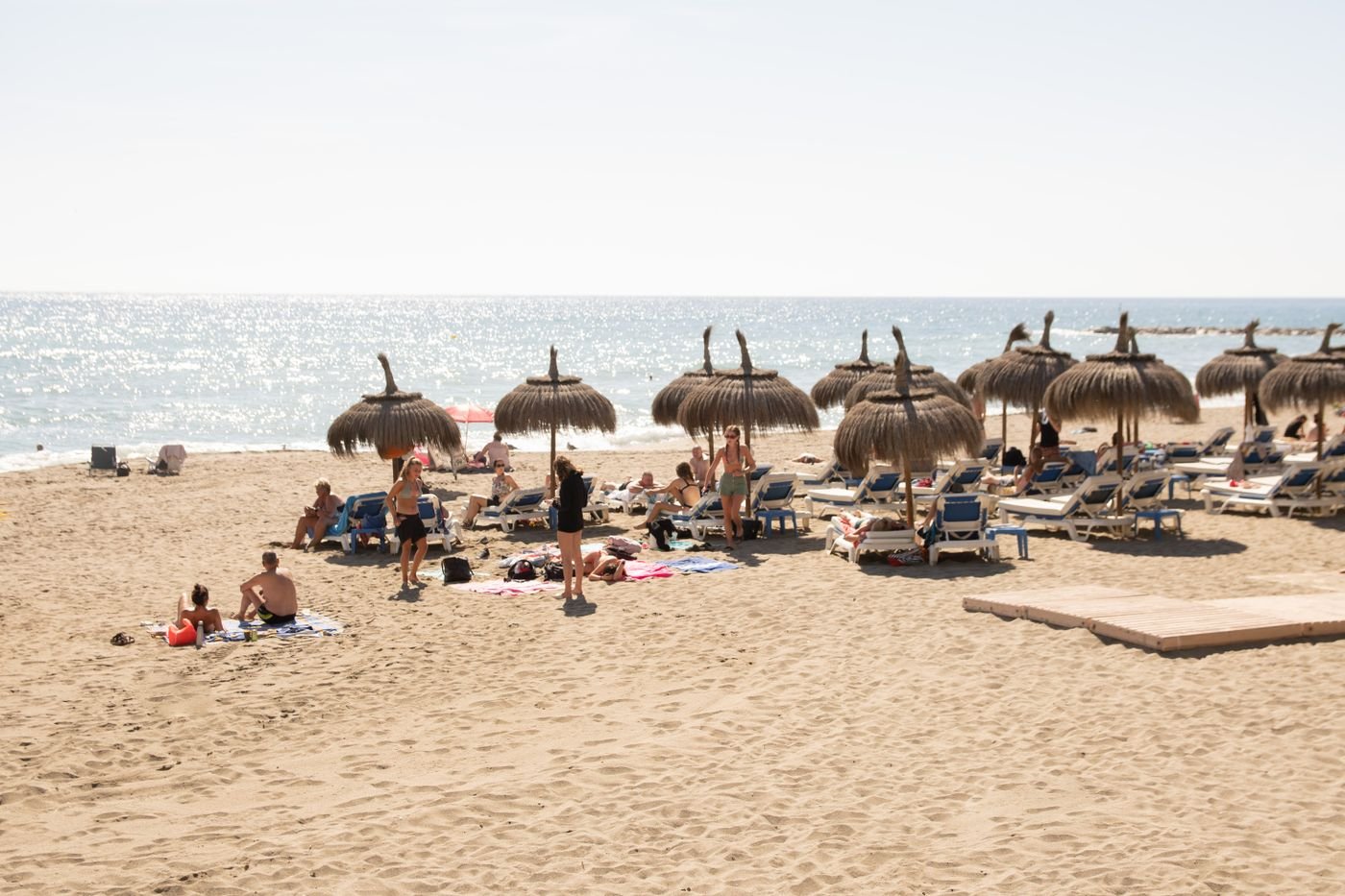 Visitors on a Marbella beach with straw umbrellas