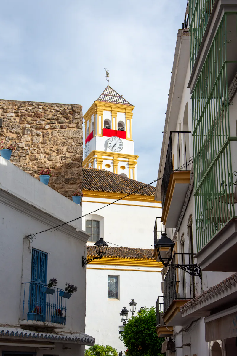 White church tower with clock seen from a narrow street in Marbella Old Town