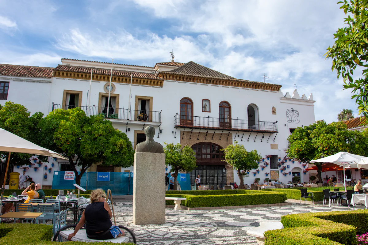 Historic white building with sundial and statue on Plaza de los Naranjos in Marbella Old Town