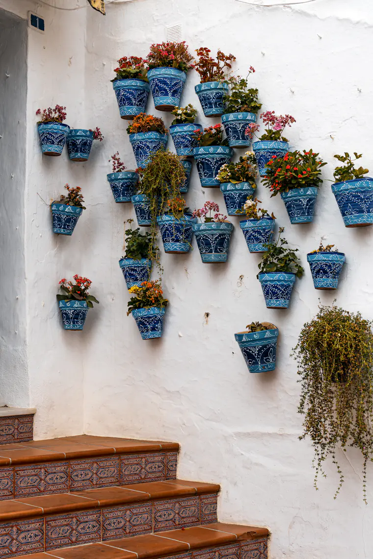 Blue flower pots on a white wall beside steps in Mijas